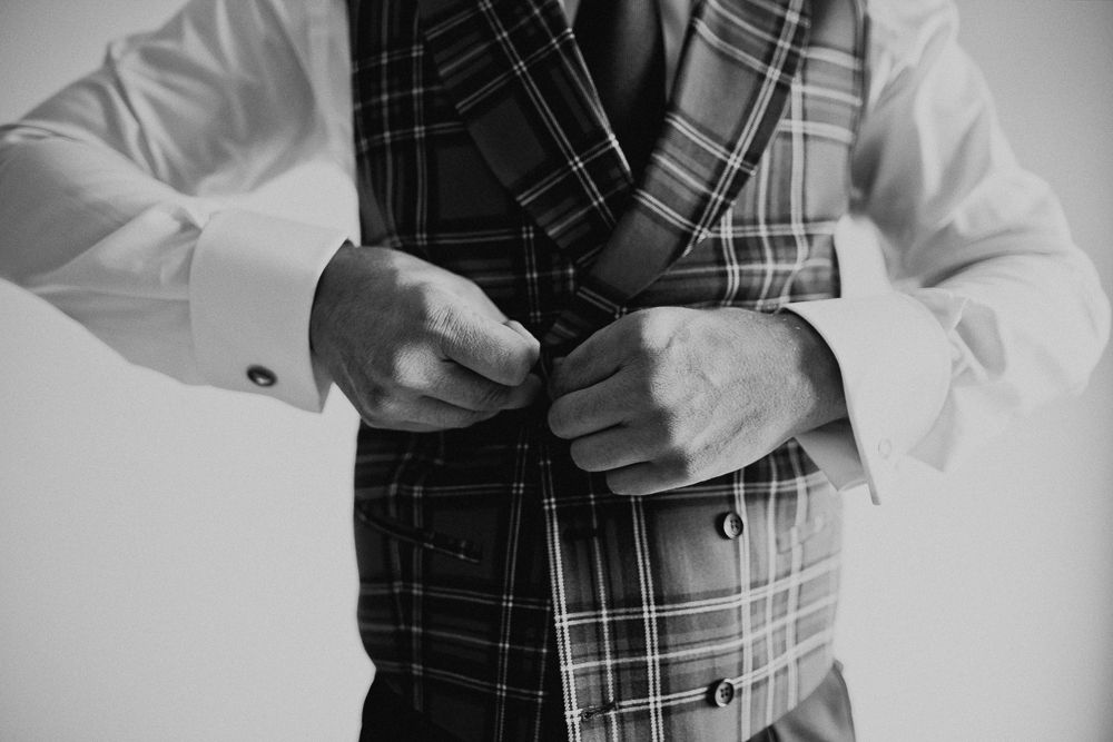 Close-up shot of hands buttoning a plaid waistcoat with white dress shirt.