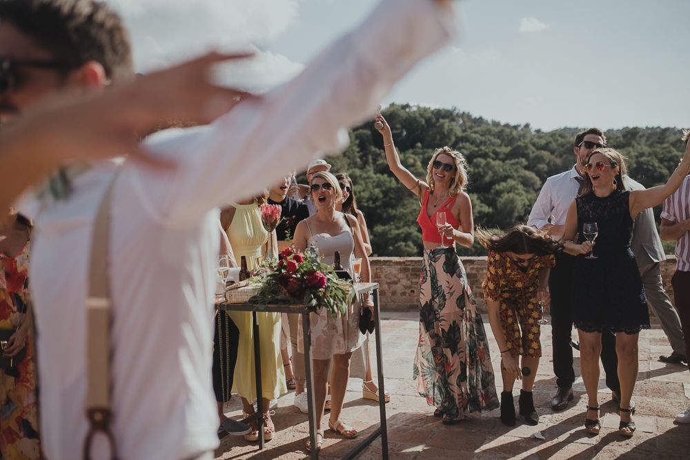 Wedding guests dancing and celebrating outdoors with arms raised in joyful celebration.