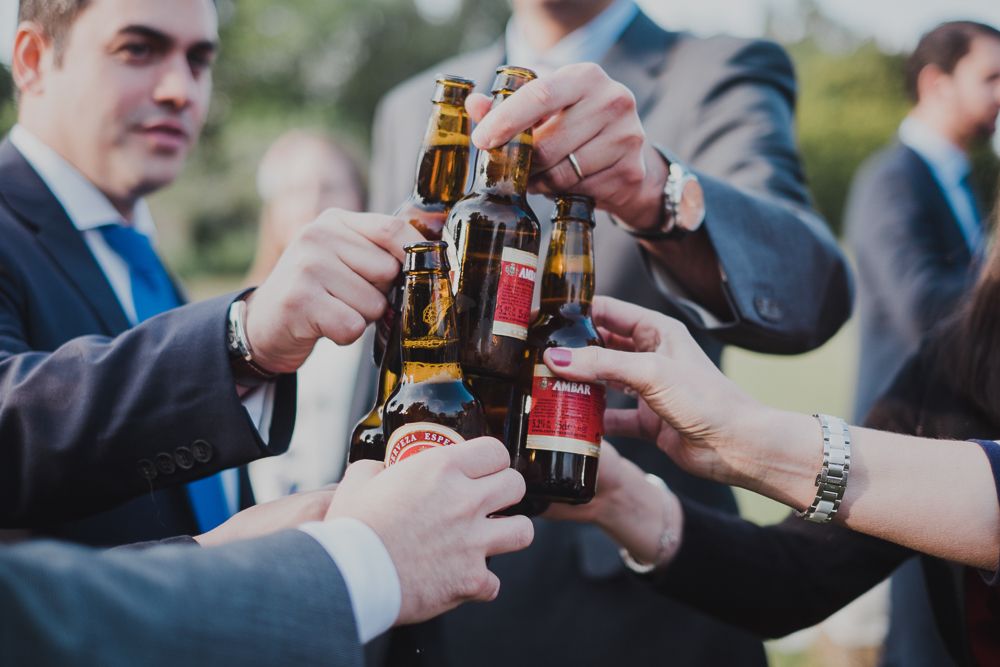 Beer bottles clinking in a celebratory toast at an outdoor wedding reception.