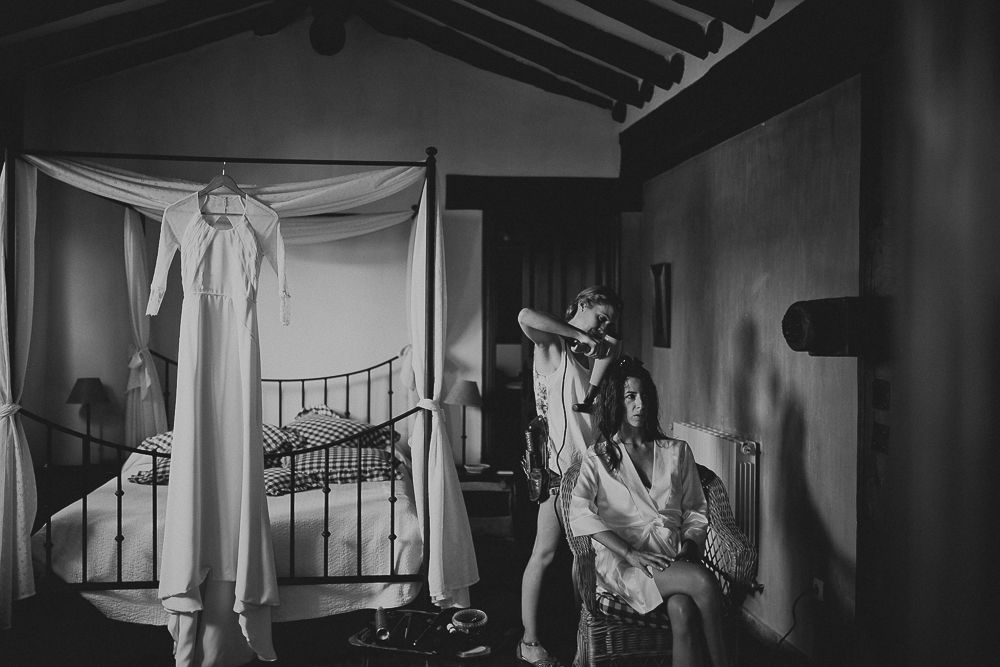 People preparing in a rustic bedroom with exposed beams and hanging white fabric.