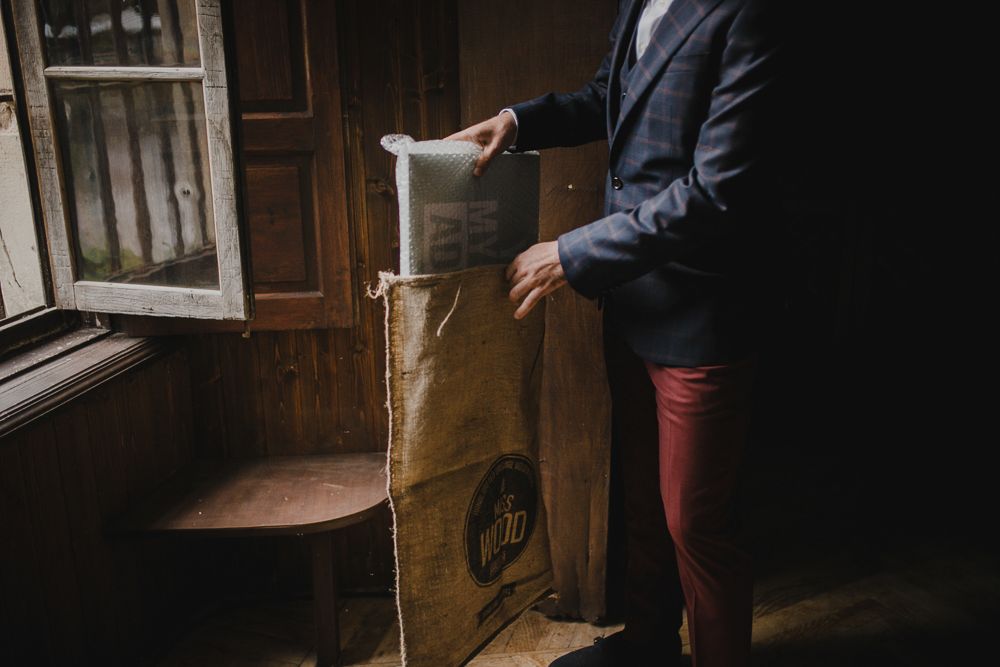 Person in blue suit and red pants examining vintage objects by window.