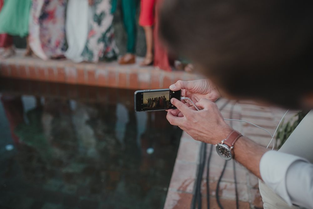Guest capturing wedding moments on smartphone at outdoor reception.