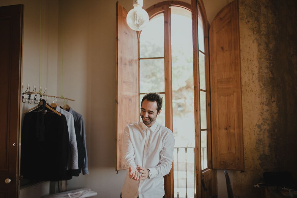 A person in a white shirt stands thoughtfully by a window in a dressing room.