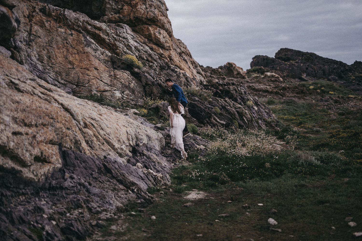 Figure in white clothing exploring steep rocky cliffs on a cloudy day.