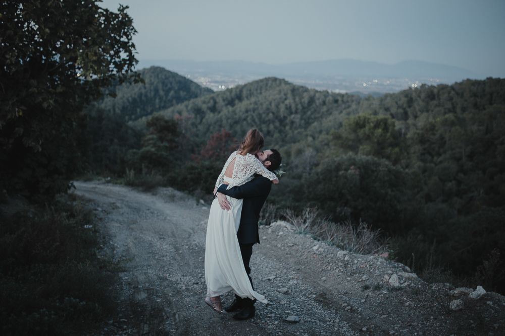 Couple embraces on a mountain path with scenic valley views in the background.