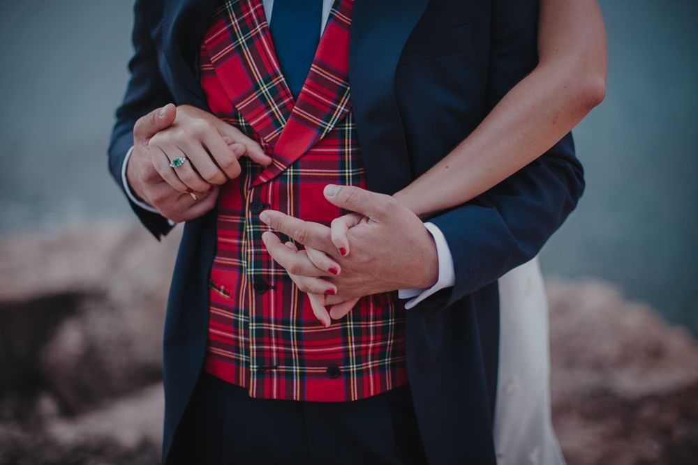 Close-up of hands with rings against red plaid vest and navy suit jacket.