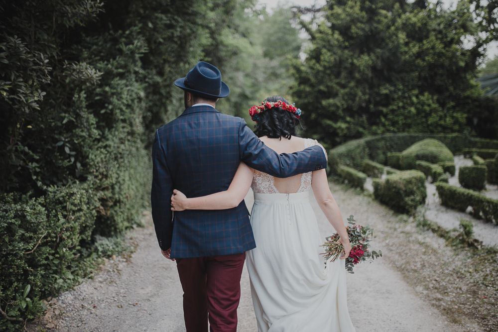 A couple walks arm in arm down a garden path at their wedding.