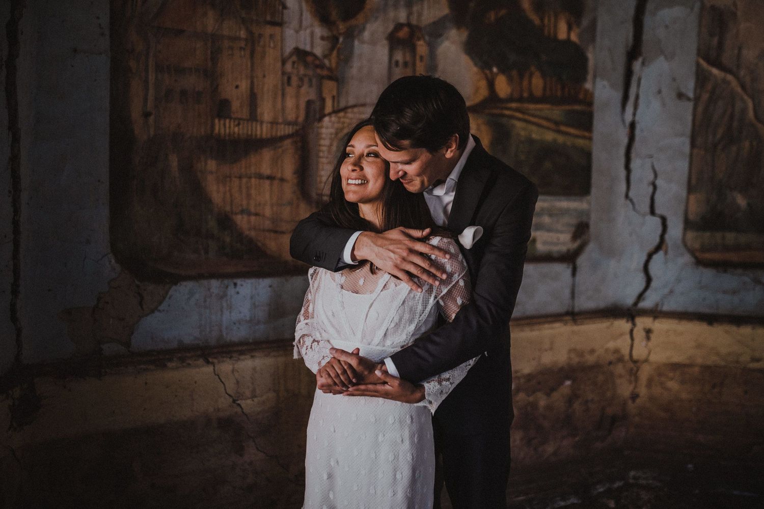 Intimate moment between couple in formal attire against rustic wall with murals.