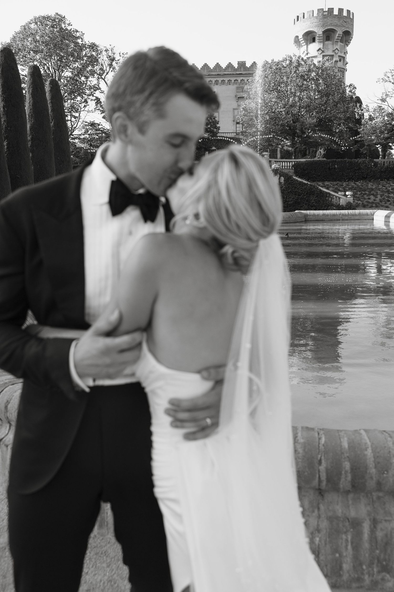 Black and white romantic wedding portrait with castle turrets and pool in background.