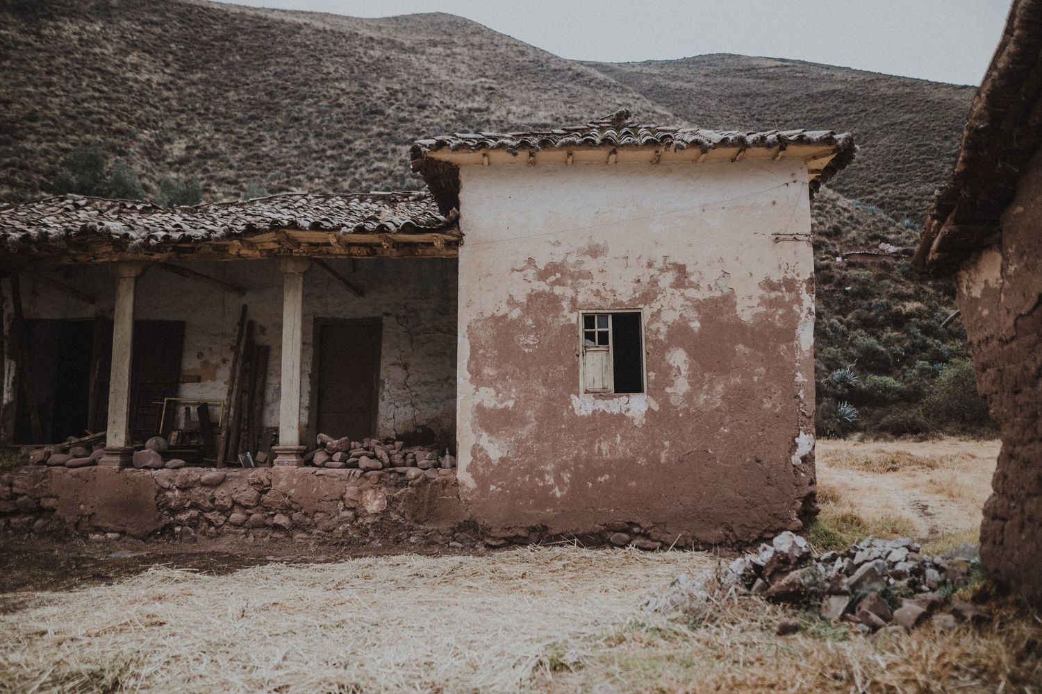 Weathered adobe building with peeling pink walls and columns stands against barren mountain landscape.