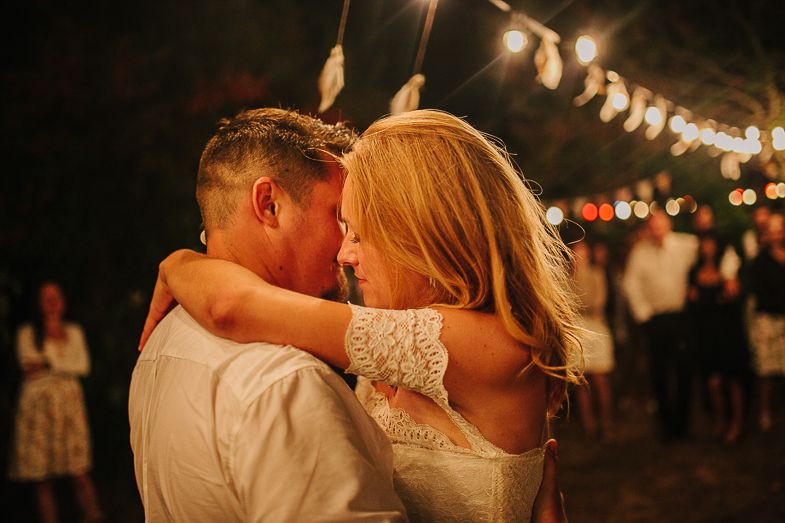Couple sharing an intimate dance moment under warm string lights at an outdoor celebration.