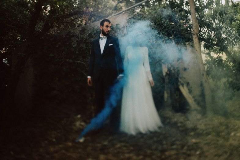 Artistic wedding photo with smoke effects surrounding a couple in a moody forest setting.