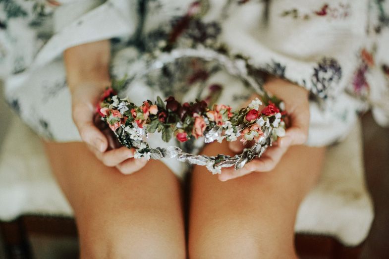 Delicate floral crown with red and white flowers held against a light fabric background.