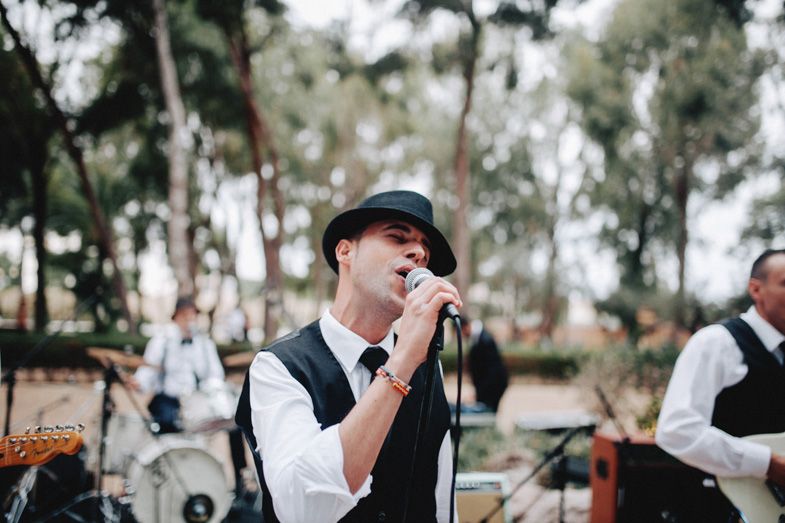 Wedding band vocalist performing outdoors under eucalyptus trees.