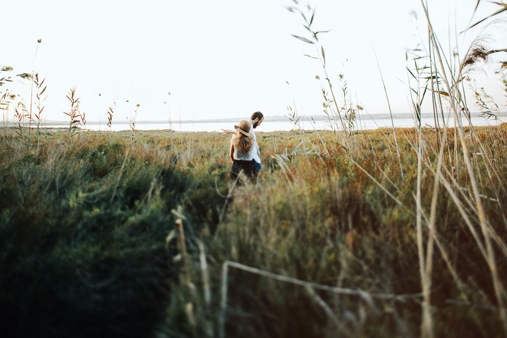 Figure walks through tall grass and reeds in a serene coastal landscape during golden hour.