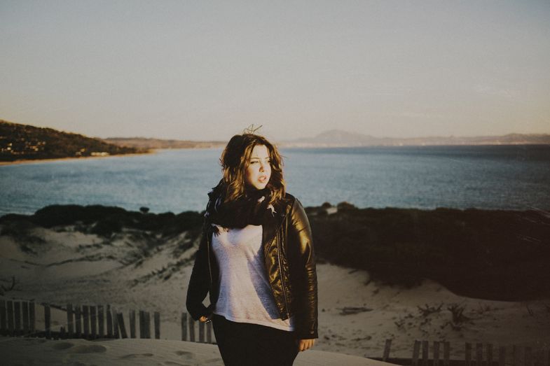 Person in casual attire standing on coastal cliffside with water view.