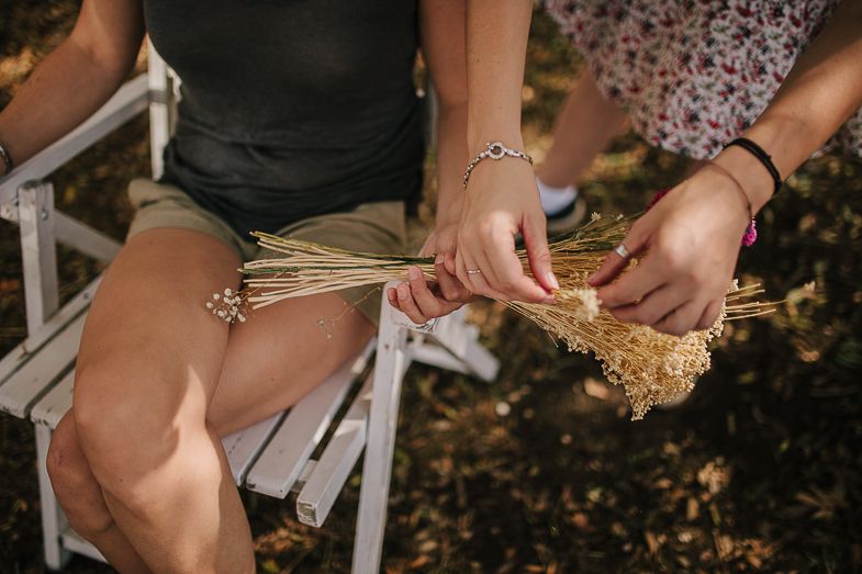 Hands holding dried wheat bundles while seated outdoors.