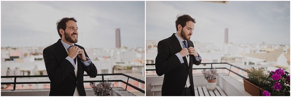 Groom adjusting his tie on a rooftop terrace with city skyline in background.