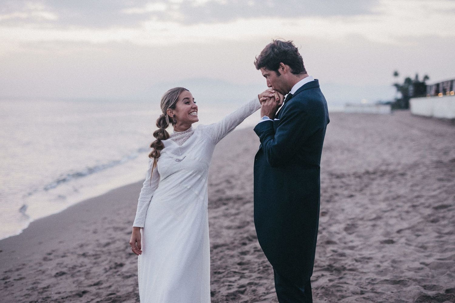 Emotional wedding moment between couple on beach with overcast sky.