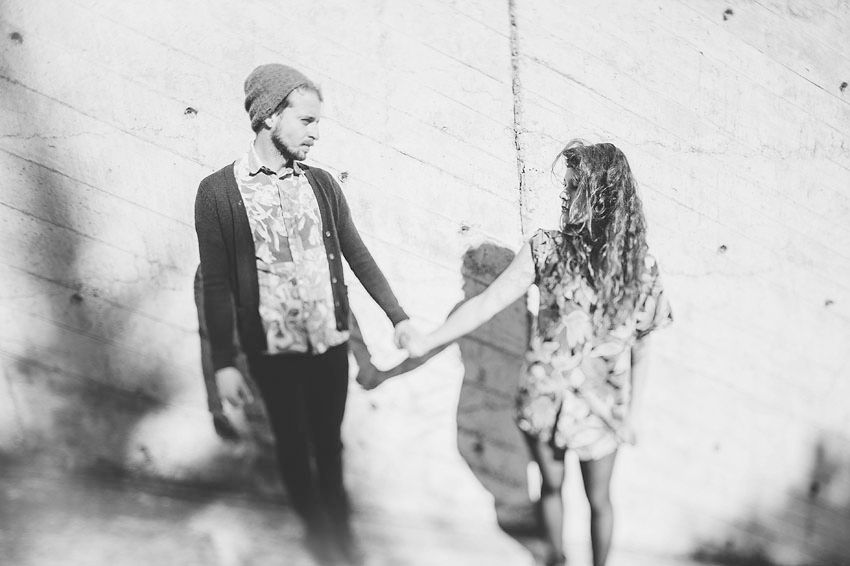 Black and white photo of two people holding hands against a weathered wall.