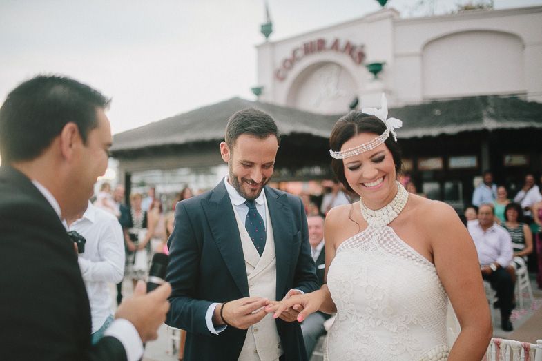 A wedding ceremony taking place outdoors with guests watching the ring exchange.