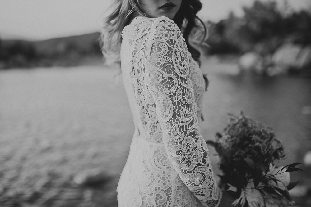 Black and white detail of lace wedding dress sleeve against water backdrop.