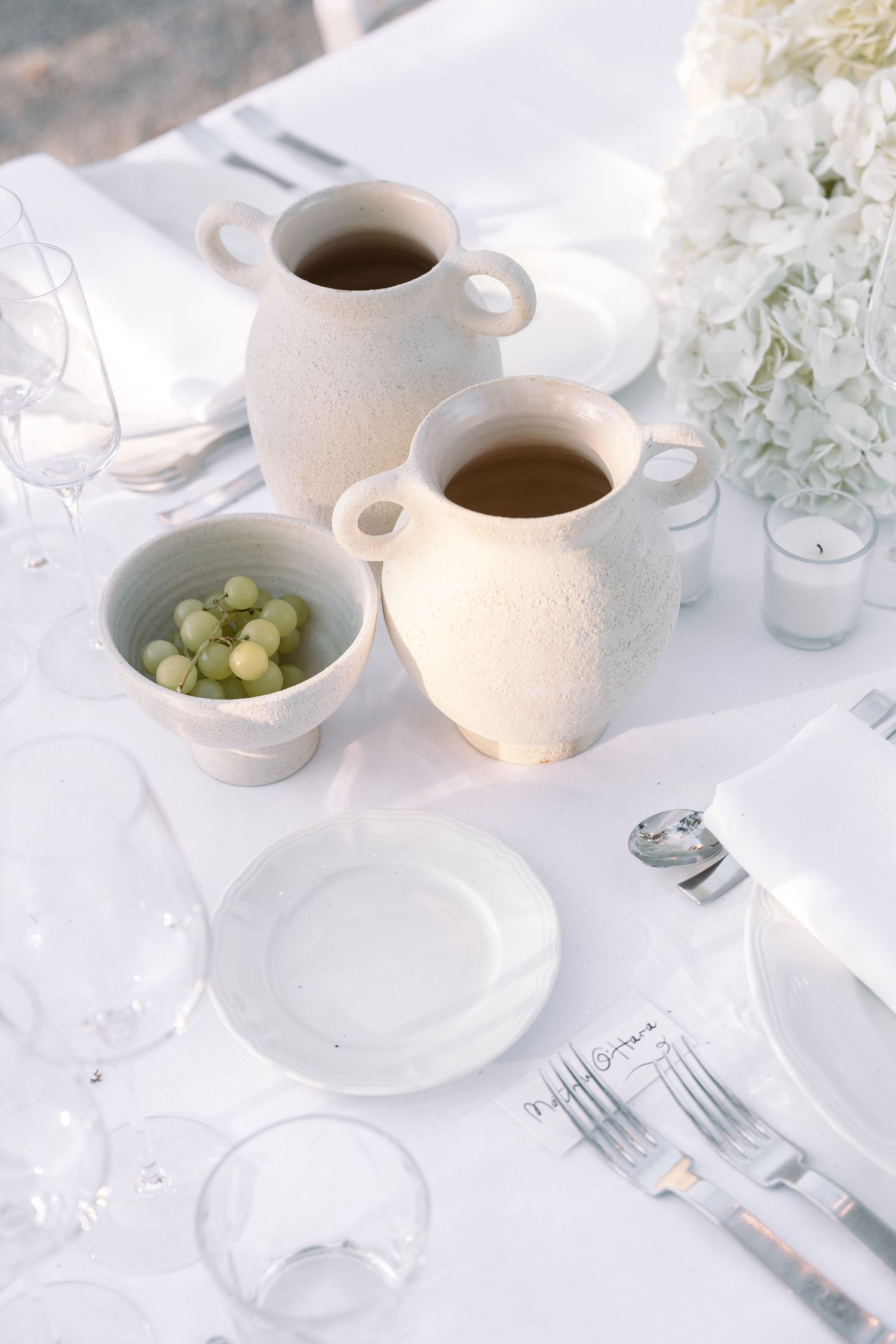 White minimalist table setting with coffee cups, grapes and delicate place settings.