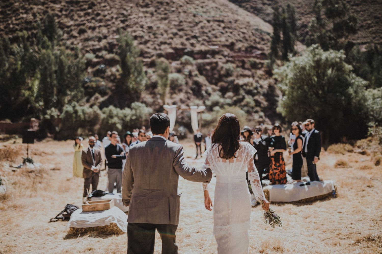 A wedding ceremony procession in a desert landscape with mountains and cypress trees.