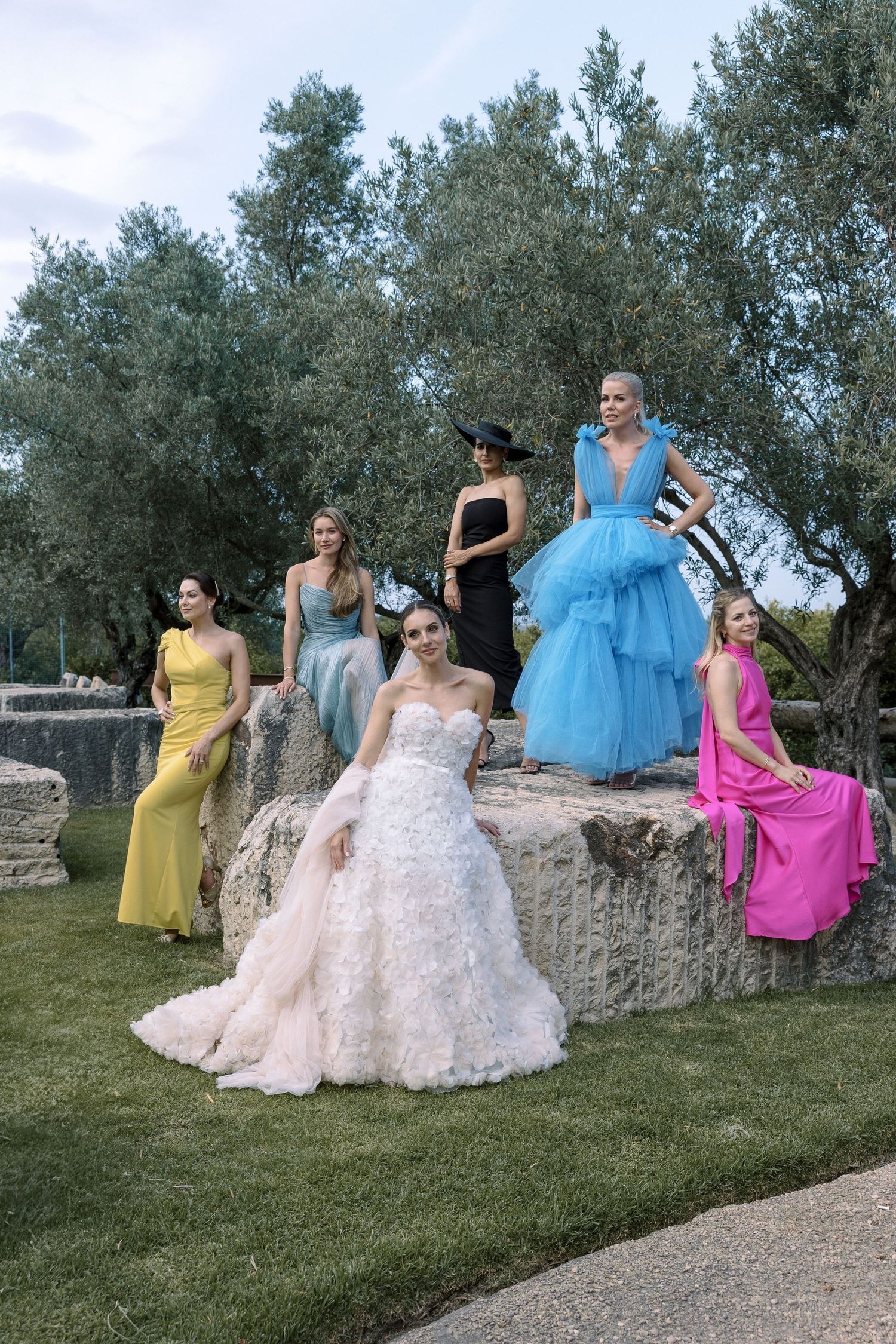 A group photo featuring bridesmaids in colorful gowns posed on stone steps in a garden setting.