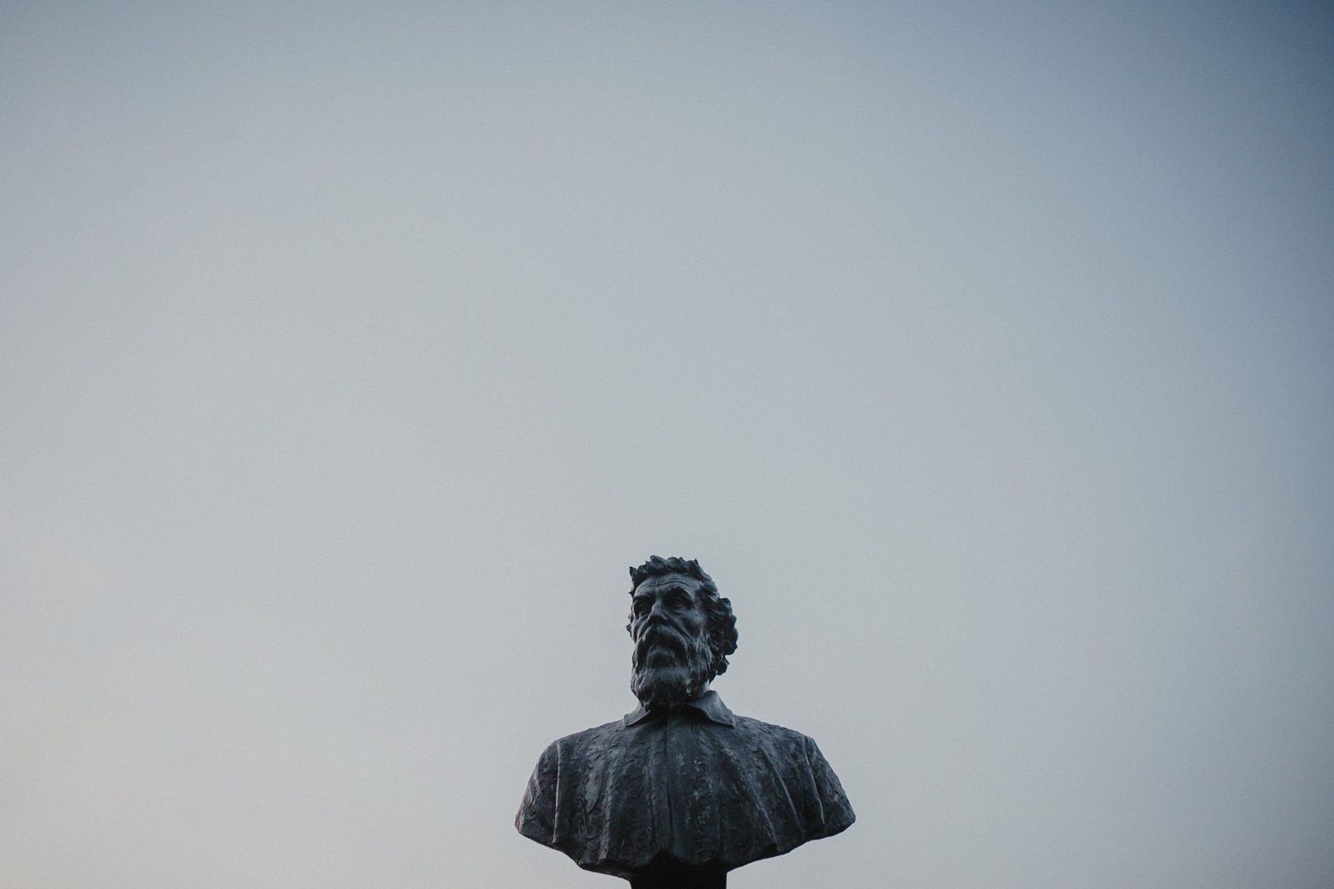 Bronze bust statue silhouetted against a pale sky in Florence.