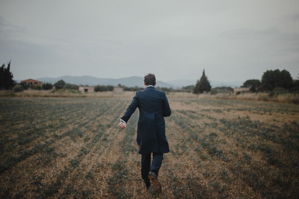 A figure in a blue suit walks alone across a misty rural field.