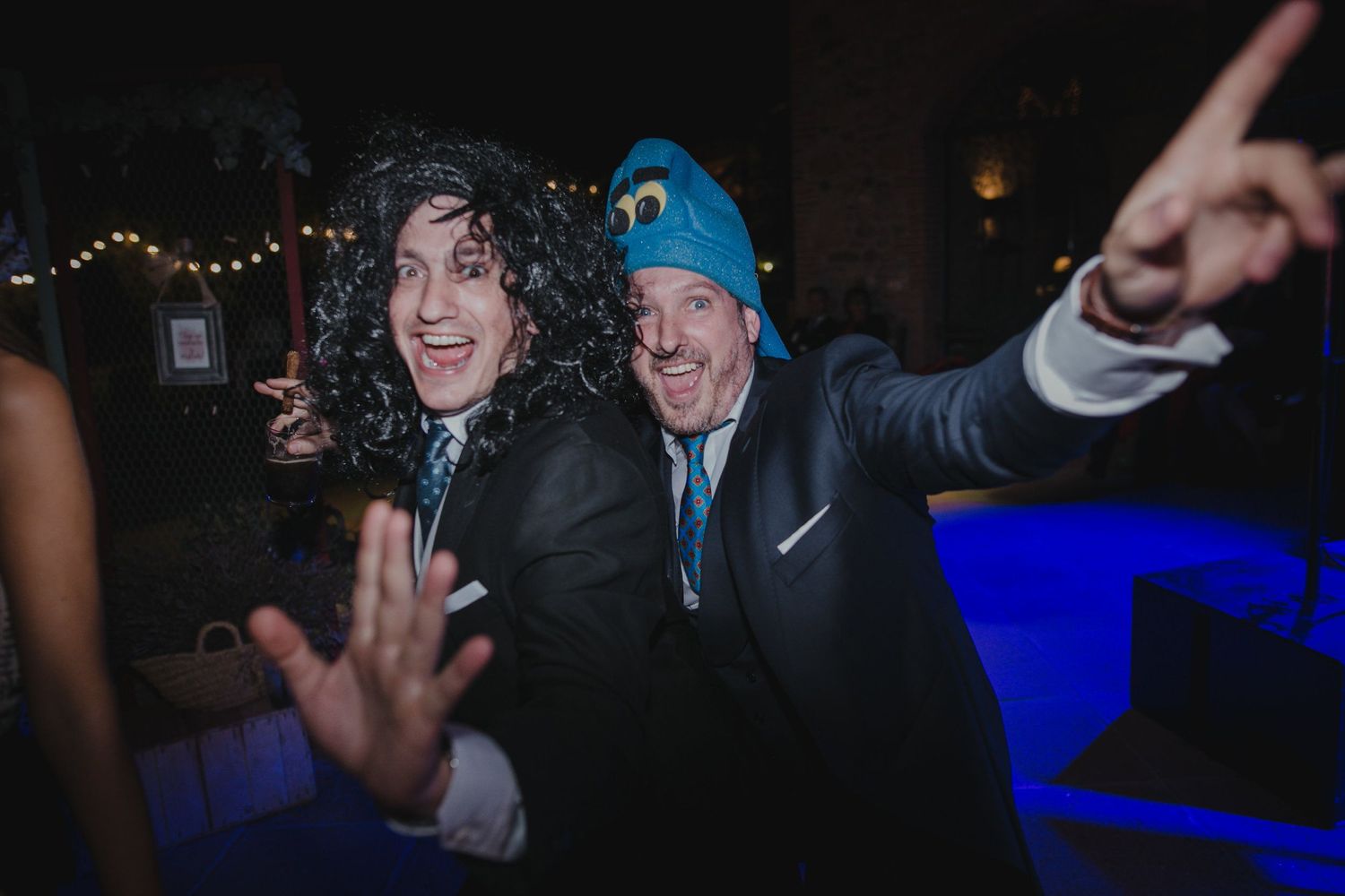 Wedding party guests dancing enthusiastically at night with blue lighting.