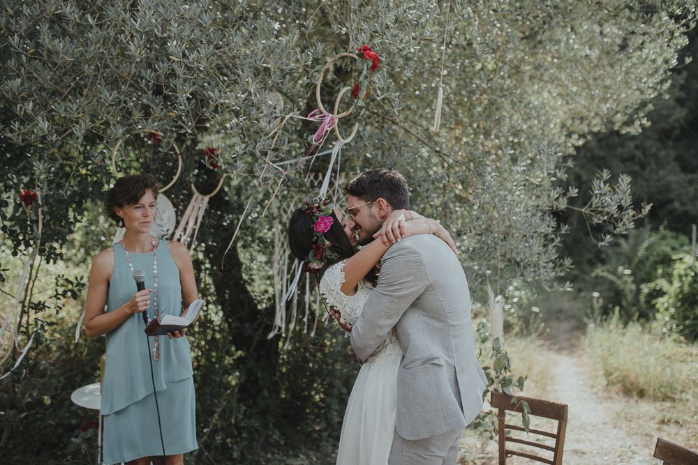 A romantic outdoor wedding ceremony under olive trees with red floral decorations.