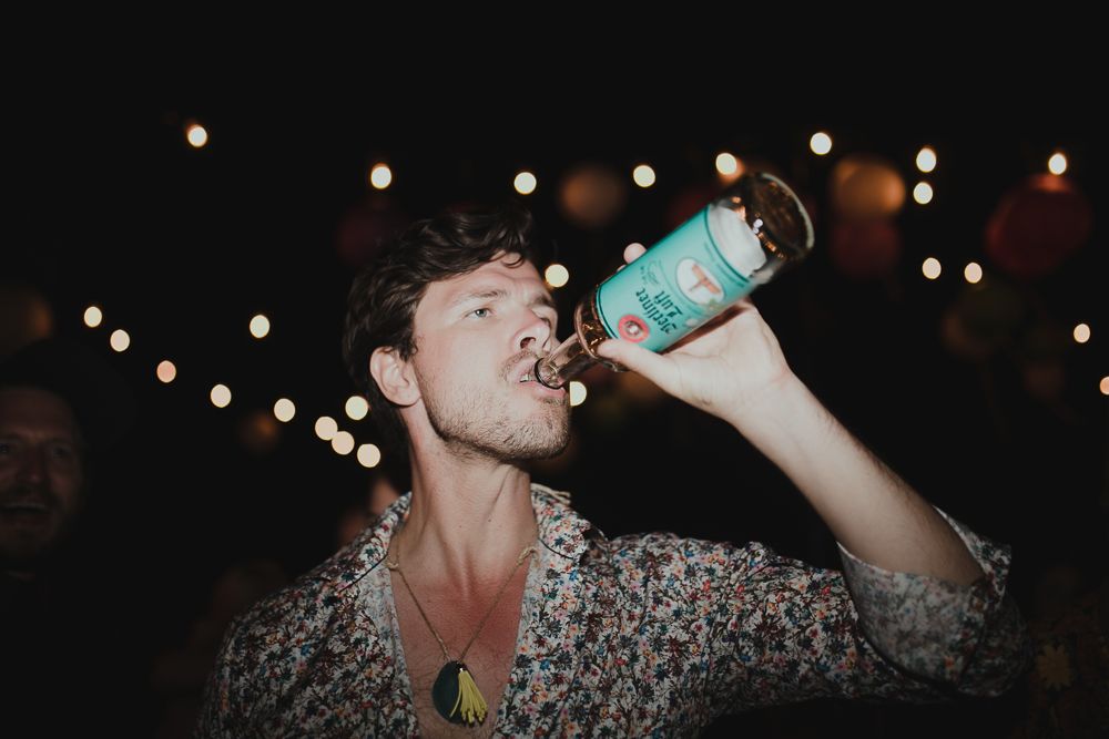 Person in floral shirt drinks from blue cup under twinkling night lights.