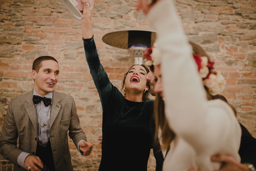 Group celebrates joyfully against rustic brick wall at wedding reception party.