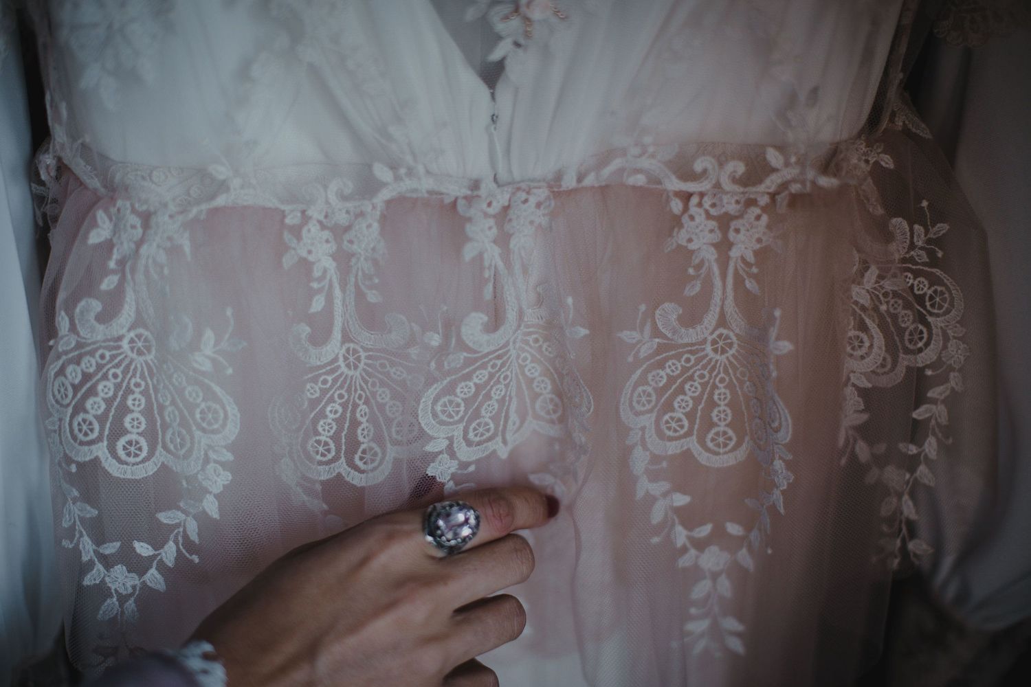 Close-up of an elegant ring against intricate white lace embroidery details.
