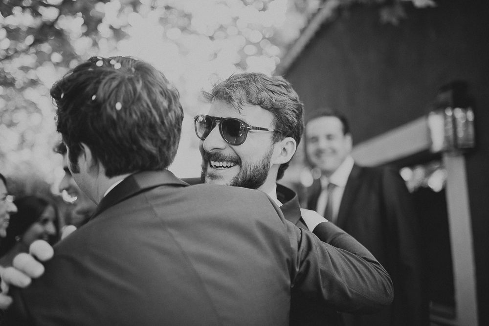 Guest in sunglasses embraces someone during outdoor wedding celebration.