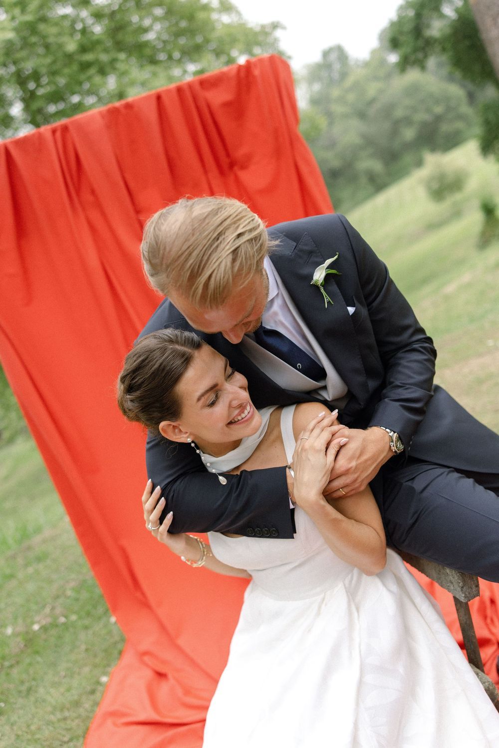 Romantic wedding portrait series against a bright red backdrop in a natural setting.