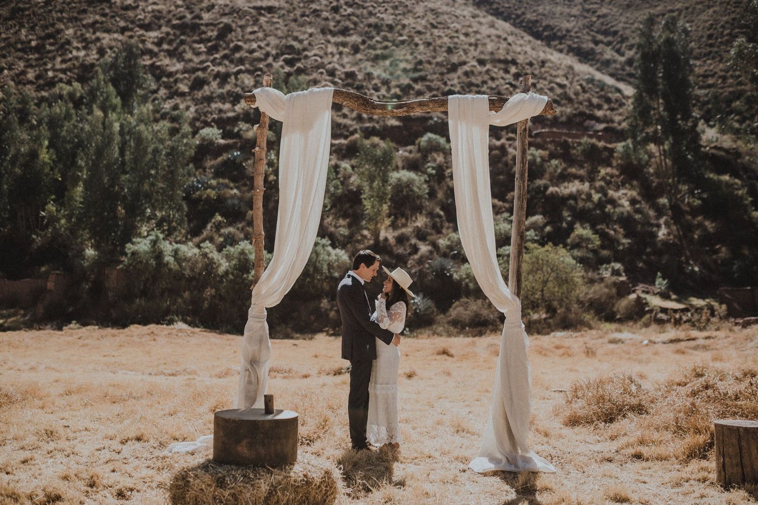 Couple standing beneath white draped wedding arch in desert setting.