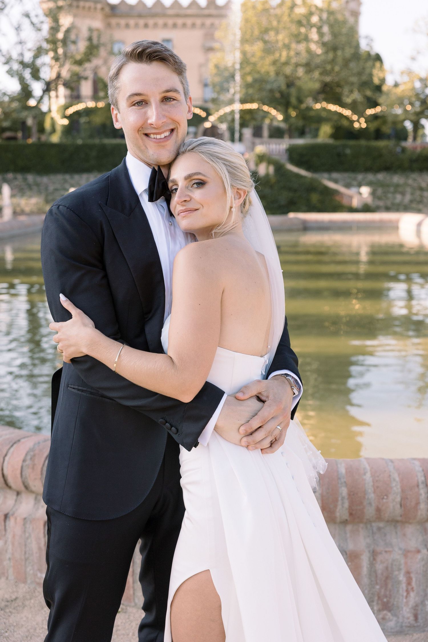 Elegant wedding portrait by a reflecting pool with castle-like venue in background.