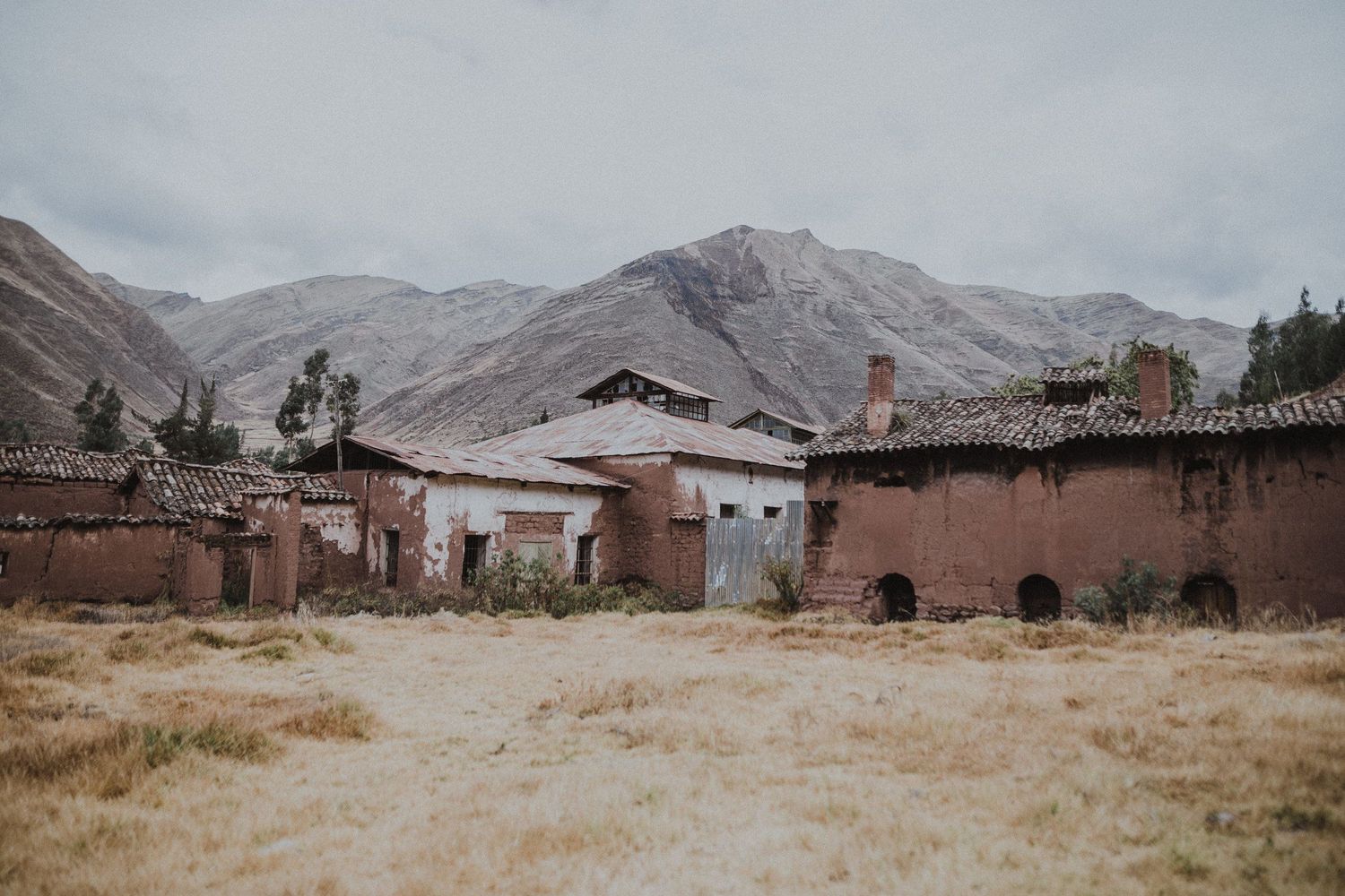 Weathered adobe buildings with metal roofs against stark mountain landscape.