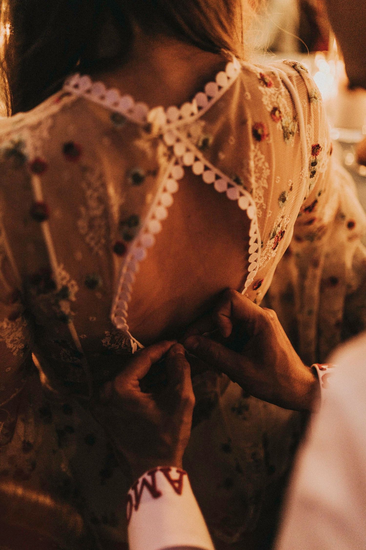 Close-up detail of a delicate lace dress with pom-pom trim and floral patterns in warm lighting.