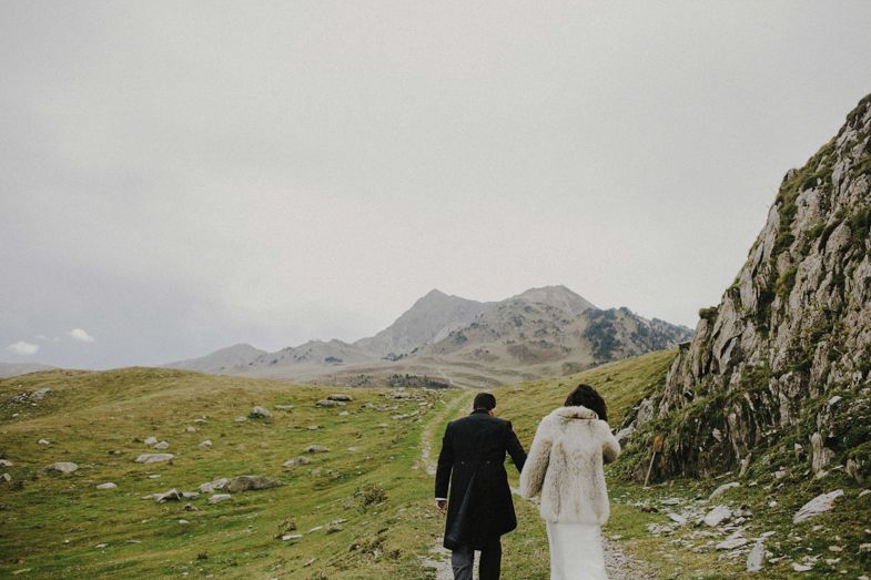 A couple in wedding attire stands against a dramatic mountain landscape.
