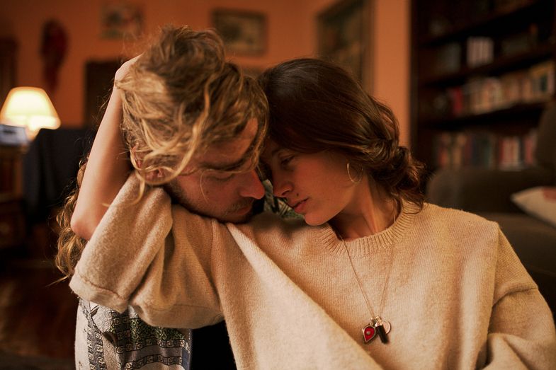 Intimate moment captured in warm lighting with person wearing cream sweater on couch.