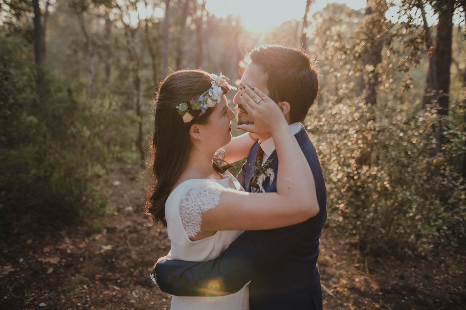A romantic sunset engagement photo of a couple in a wooded area with soft lighting.