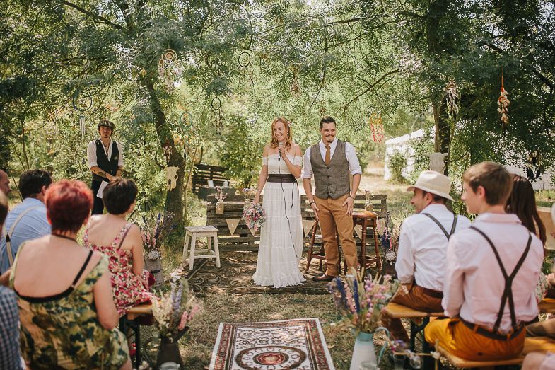 Rustic woodland wedding ceremony with vintage decor and standing guests.