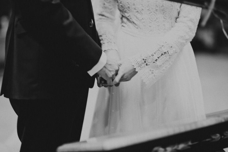 A black and white detail shot of a couple holding hands during their wedding ceremony.