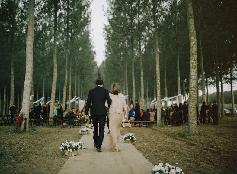 Wedding couple walking down a tree-lined path with guests and decorations in the background.