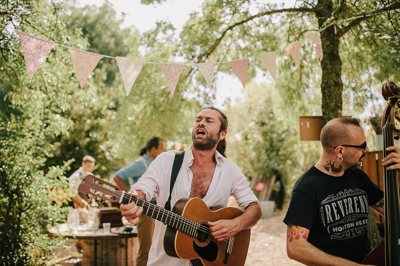 Musicians performing with acoustic guitar at an outdoor wedding reception under string lights.