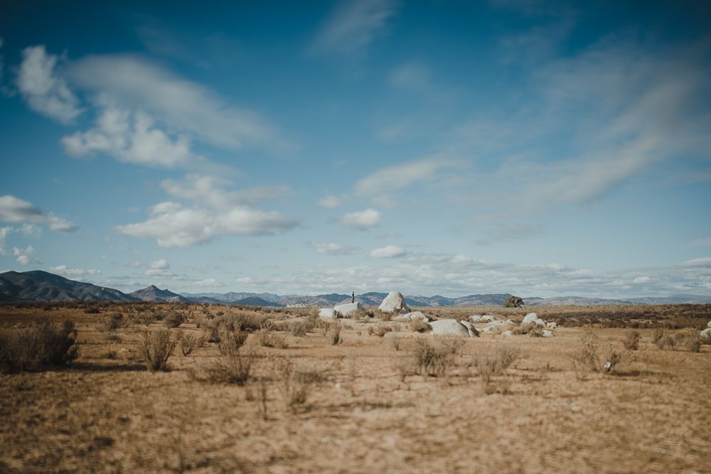 Desert landscape with mountains and scattered buildings in the distance under blue skies.